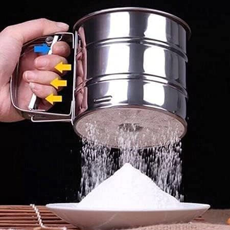 Metal sifter being used to sift flour into a bowl with a dark background