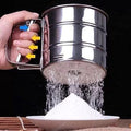 Metal sifter being used to sift flour into a bowl with a dark background