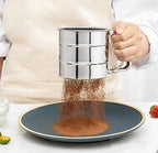 Person sifting coffee grounds into a bowl using a metal sifter.