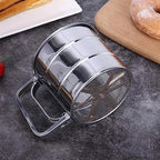 Metal flour sifter on a gray surface with pastries in the background