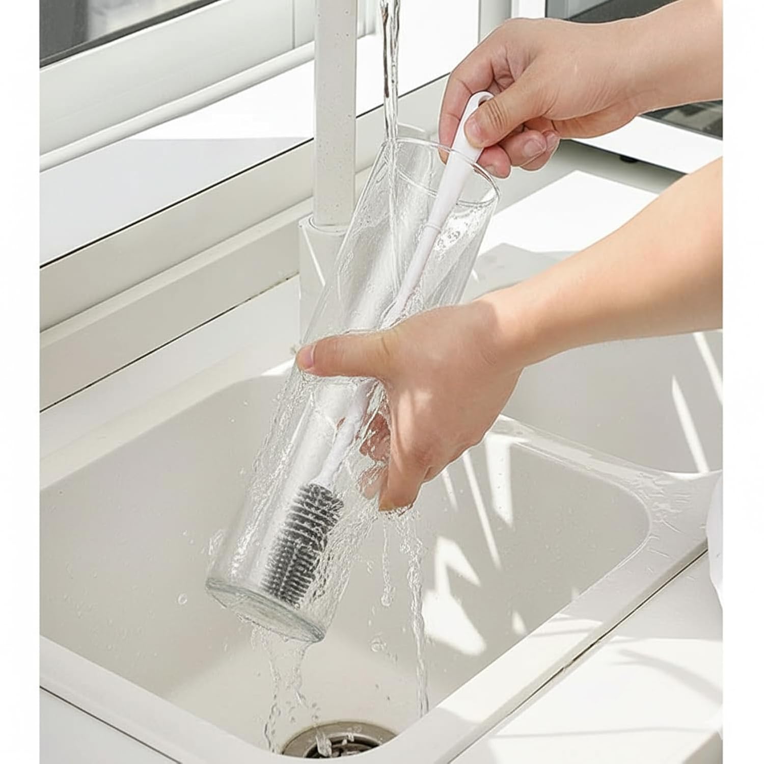 Person rinsing a clear bottle with a brush under running water in a kitchen sink.