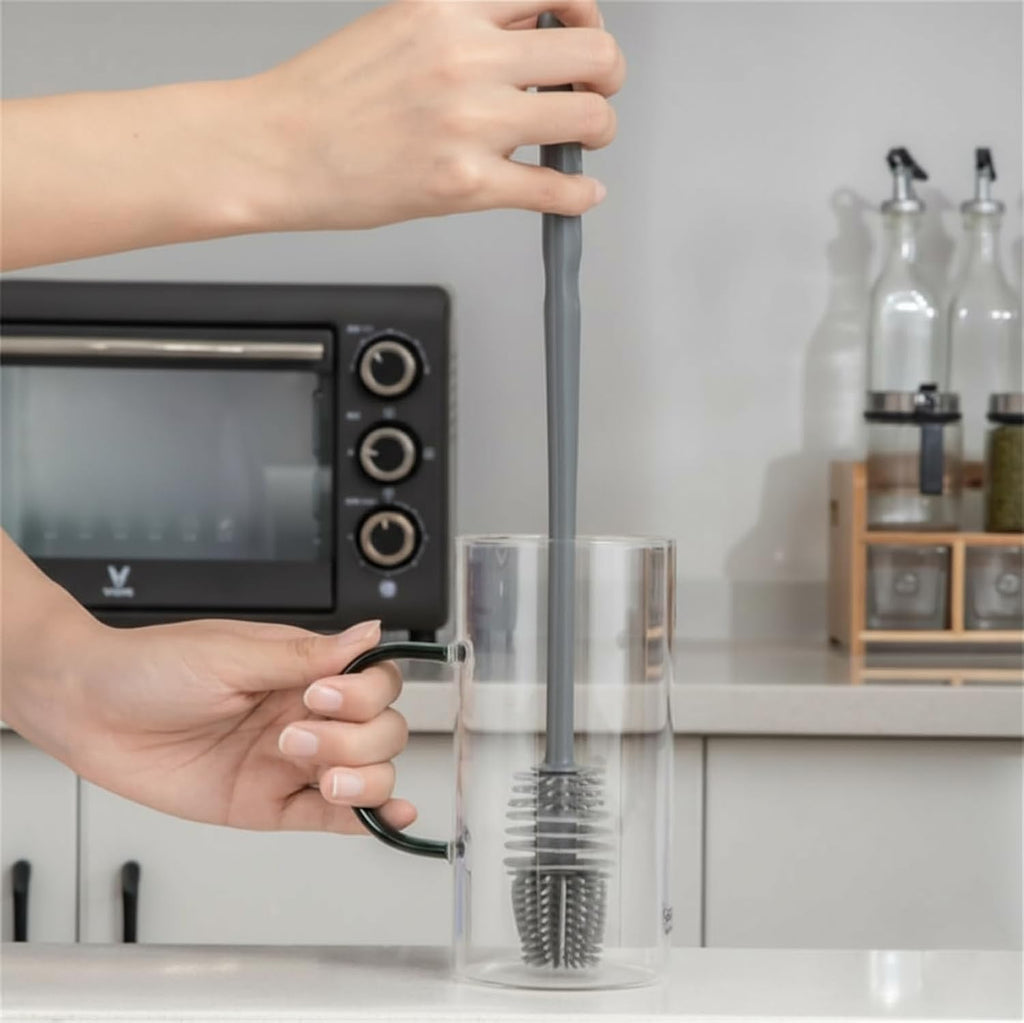 Person using a kitchen brush to clean a glass container in a kitchen setting.
