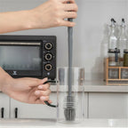 Person using a kitchen brush to clean a glass container in a kitchen setting.