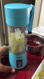 Blue portable blender with fruits inside on a red surface